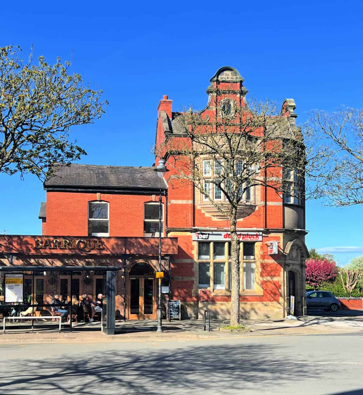 Street view of Birkdale on a sunny day, showing a red brick betting shop and a cafe with people sat outside