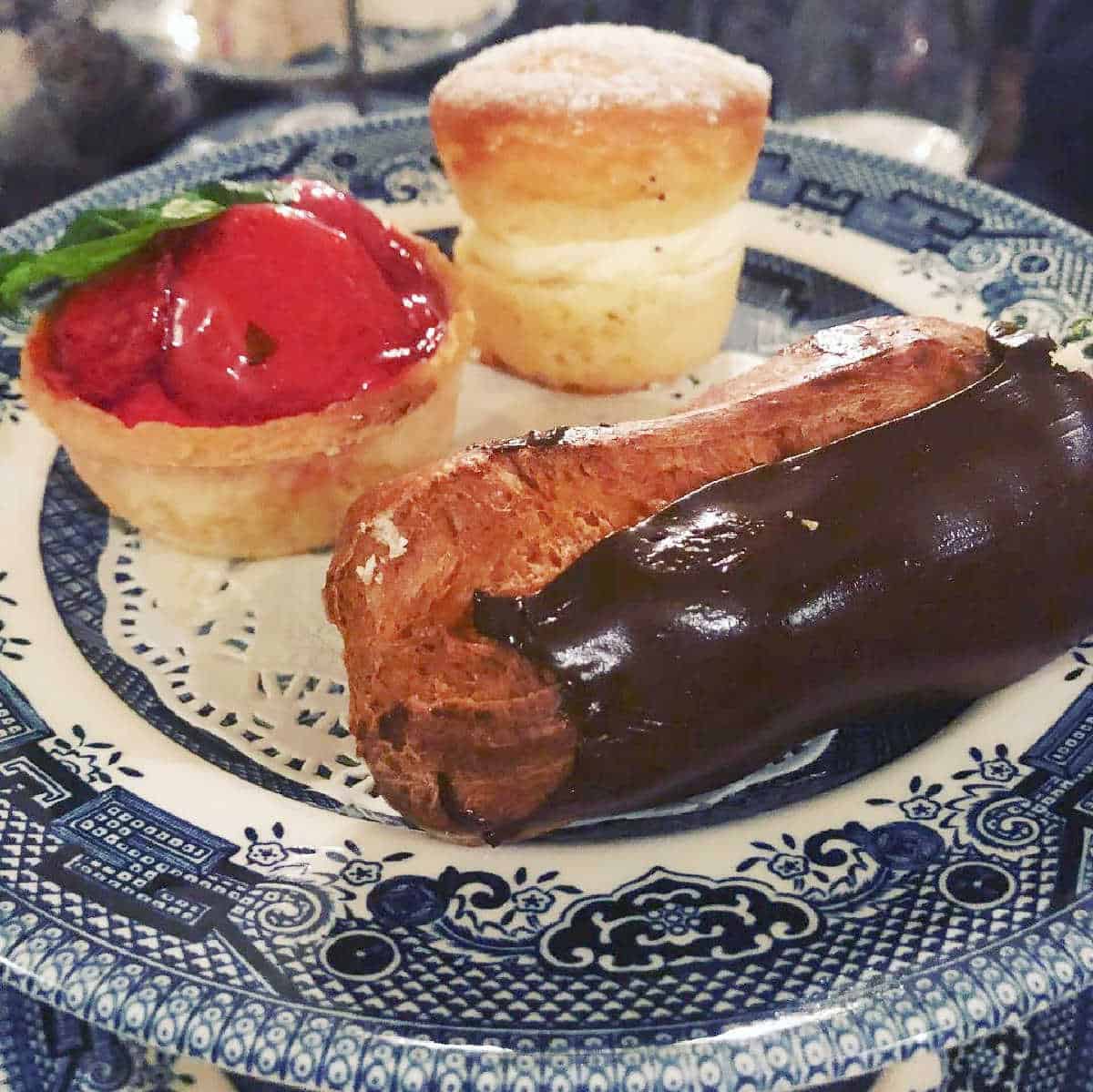 blue and white plate with a selection of 3 cakes including a chocolate eclair, a strawberry tart and a victoria sponge for a post on Mother's Day events taking place in Liverpool and Merseyside