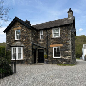 Front view of Newby Bridge House from the main road with gravel parking space leading round to the parking area at the rear.